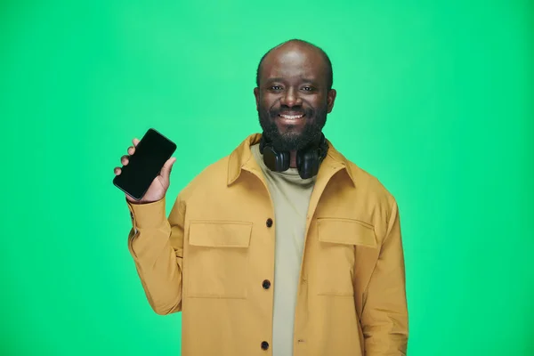 在绿色背景下展示手机屏幕时 非洲裔美国人对着相机微笑的肖像 — 图库照片