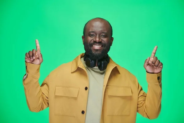 非洲裔美国人的画像 头戴耳机 举起手来 对着站在绿色背景上的相机微笑 — 图库照片