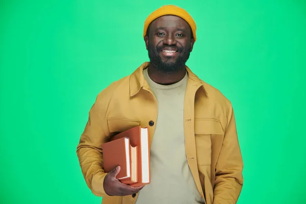 アフリカ系アメリカ人男性の肖像本を持ち カメラに向かって笑っている姿が緑の背景に立っている — ストック写真