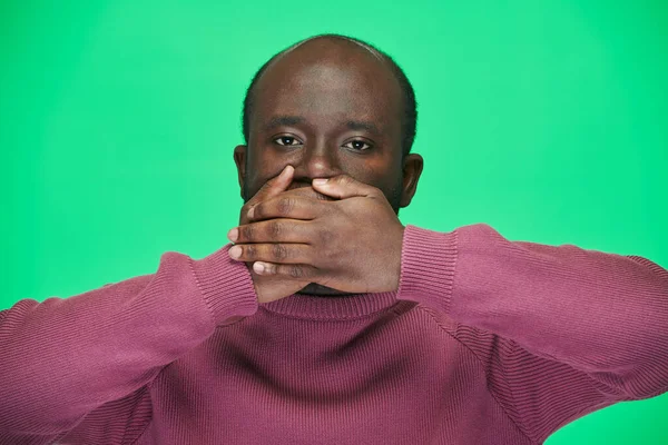 Портрет Афроамериканца Смотрящего Камеру Закрывающего Рот Руками Зеленом Фоне — стоковое фото