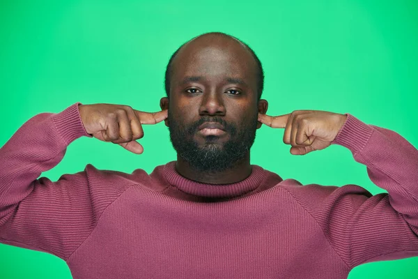 緑の背景にカメラを見て大きな音から耳を覆うアフリカ系アメリカ人の男性の肖像 — ストック写真