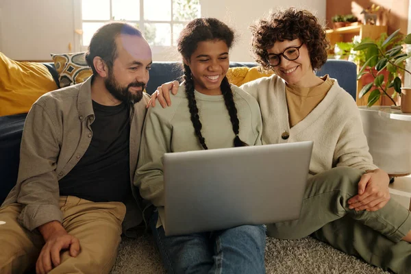 Happy family watching funny video on laptop together with their adopted daughter during leisure time at home