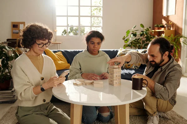 父亲和他的养女一起玩棋盘游戏 而母亲则用她的智能手机 坐在家里客厅里 — 图库照片