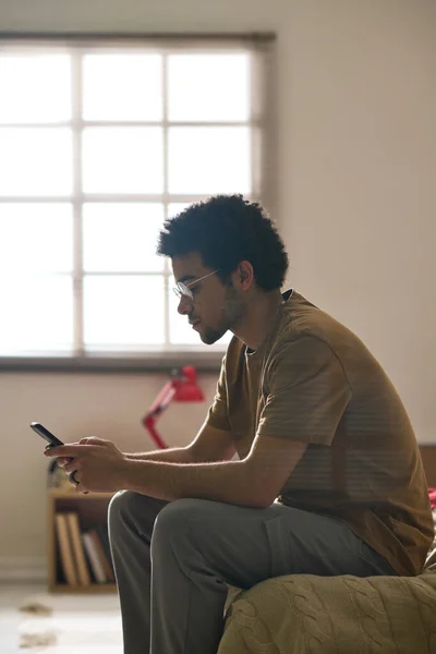 Imagem Vertical Triste Homem Comunicando Smartphone Enquanto Está Sentado Cama — Fotografia de Stock