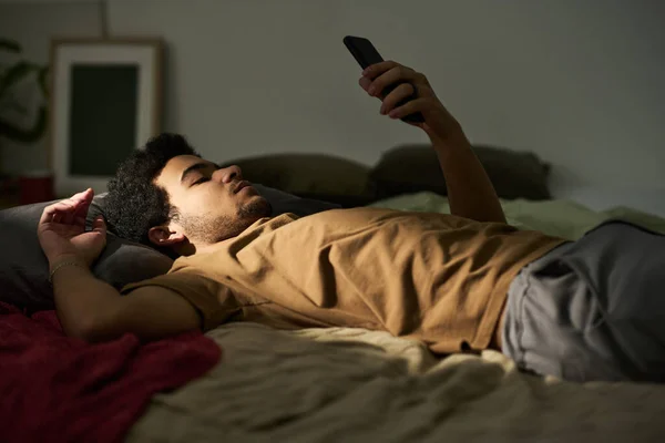 Jovem Deitado Cama Sem Humor Usando Seu Smartphone Ele Fica — Fotografia de Stock