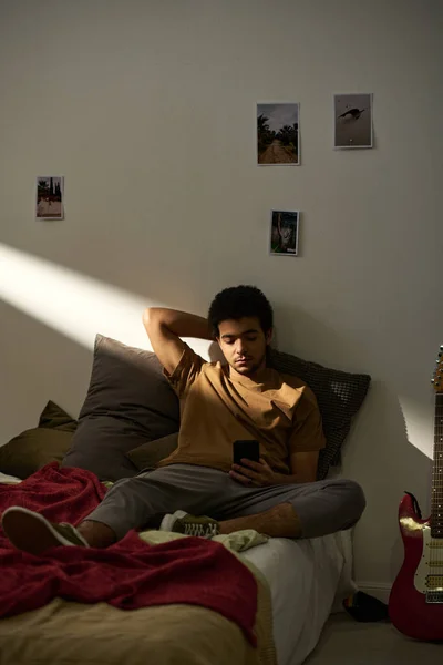 男青年躺在卧室里躺在床上用智能手机阅读信息的垂直图像 — 图库照片