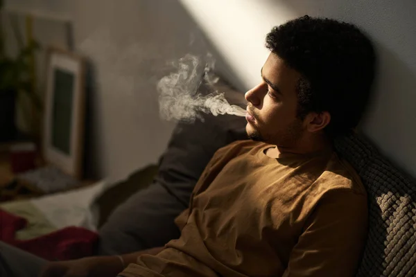 憂うつな喫煙の若い男と彼の問題だけで部屋に座って考えて — ストック写真