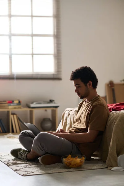 Genç Bir Adamın Yerde Oturup Çip Yerken Bilgisayarını Kullanarak Iletişim — Stok fotoğraf