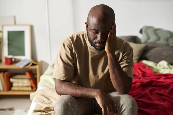 アフリカ系アメリカ人の男は目を閉じてうつ病でベッドに座って頭痛を持っている — ストック写真