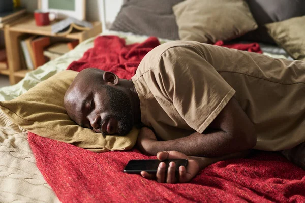 疲惫的非洲裔美国人躺在床上 手里拿着智能手机等电话 — 图库照片