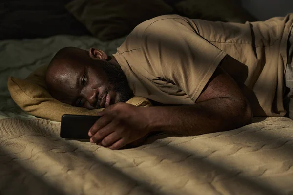 African American Melancholic Człowiek Czytanie Wiadomości Smartfonie Leżąc Łóżku Sypialni — Zdjęcie stockowe