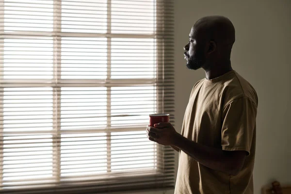早上喝咖啡时凝视着窗户的一个心事重重的非裔美国人 — 图库照片