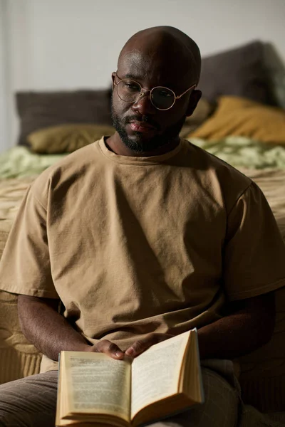 Afroamerykanin Okularach Siedzący Podłodze Zamyślonym Wyrazem Twarzy Czytając Książkę — Zdjęcie stockowe