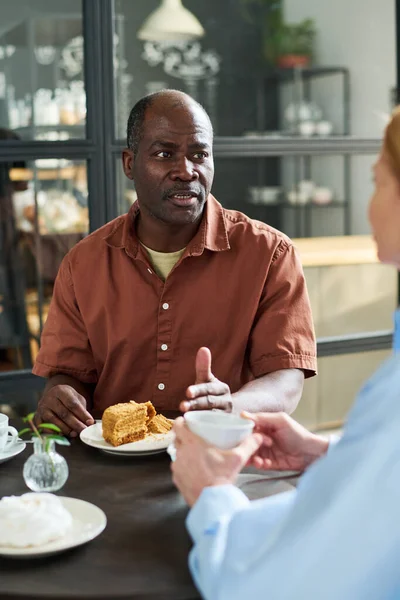 穿着棕色衬衫的成熟男人一边坐在咖啡店或餐馆的餐桌旁一边喝茶 一边和妻子说话 — 图库照片