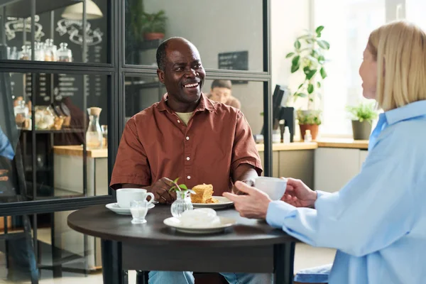 在交谈中 快乐的非裔美国男人笑着看着他的妻子 坐在咖啡馆或餐馆的餐桌旁 — 图库照片