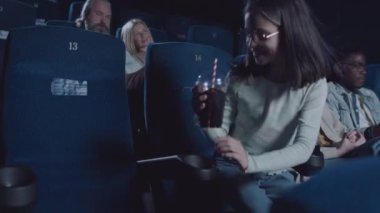 Beyaz kadın ve küçük kızı film başlamadan önce sinema salonundaki yerlerini alıyorlar.