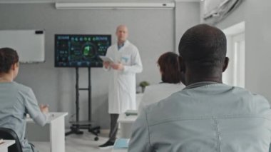 Etnik çeşitlilikte bir grup doktor masada oturup sunumuyla ilgili sorular soruyorlar.