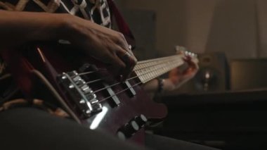 Kayıt stüdyosunda ya da konser sırasında kameranın önünde otururken elektro gitar çalan genç müzisyenin yakın çekimi
