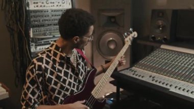 Genç Afrikalı Amerikalı müzisyen ses miksajı yaparken elektronik gitar çalıyor ve yeni müziğini stüdyoda kaydediyor.
