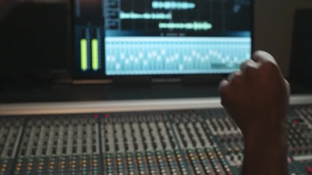 2人の若いアフリカ系アメリカ人ミュージシャンの手の近くに音のミキシングボードと録音設定の画面に対してカメラの前でパンチバンプを作る — ストック動画