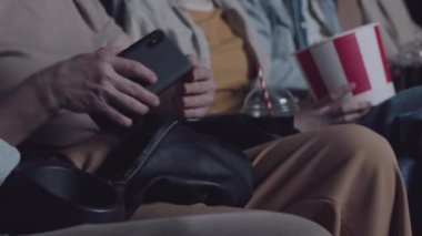 Tanımlanamayan olgun bir kadın sinemadan önce sesini kapattıktan sonra akıllı telefonunu çantaya koyuyor.