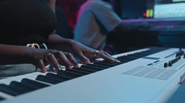 Genç siyahi bir kadının akıllı gündelik kıyafetlerini giyip elektrikli sentezleyicinin tuşlarına basarken ses mühendisiyle birlikte ses kaydını yapıp ses seviyesini ayarlamak.