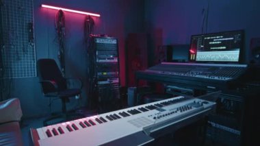 Geniş modern kayıt stüdyosu. Koltuğu duvarın yanında, neon lambalı. Müzisyen ve ses panosu için sentezleyici.