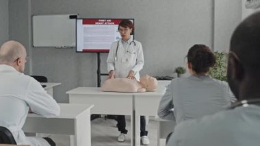 Tıbbi eğitimde ilk yardım kuralları hakkında konuşan olgun bir sağlık uzmanı, onu dinleyen çeşitli doktor ve hemşireler.