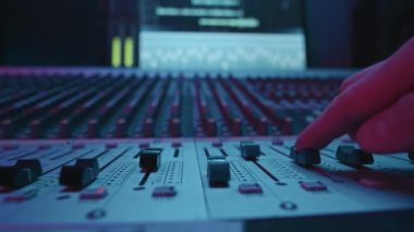 Operatör ya da müzisyenin eli, ses seviyesini yükseltirken ve sesleri ayarlarken konsolu ileri doğru hareket ettirirken yeni bir müzik oluşturup stüdyoda kaydediyor.