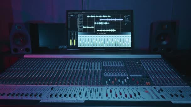 サウンドとノイズレベル 周波数波と現代のスタジオで多くのコンソールと2つのサブウーファーとワイドレコードボードに囲まれたミキシングボードの一部を示すコンピュータ画面 — ストック動画