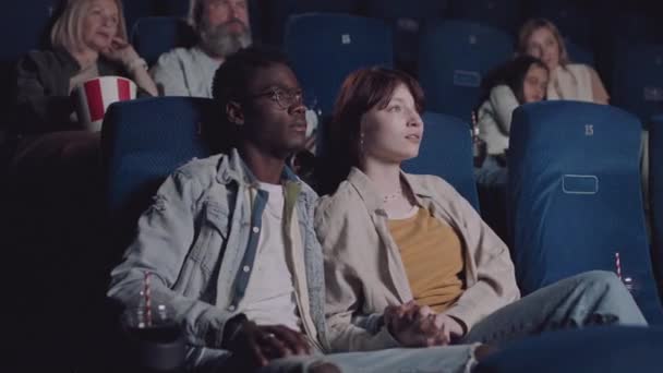 不同种族的年轻夫妇在电影院看恐怖片 年轻女人倾向于她的男朋友 — 图库视频影像