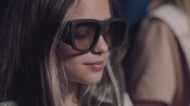 Polarize 3D gözlük takan, patlamış mısır yiyen ve sinemada film izleyen beyaz kızların seçici odak noktası.