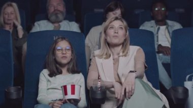 Zarif beyaz kadın ve kızı birlikte film izleyerek ve sinemada patlamış mısır yiyerek vakit geçiriyorlar.