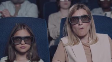 Sarışın kadın ve kızının polarize 3D gözlük takıp film izlediği, patlamış mısır yediği ve sinemada kola içtiği seçici odak noktası.