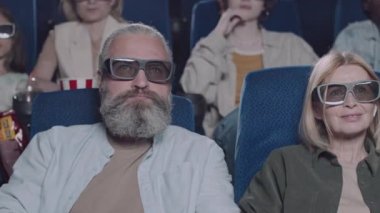 3 boyutlu gözlük takan, film izleyen, patlamış mısır yiyen ve sinemada gazoz yudumlayan olgun beyaz kadın ve erkeğin seçici odak noktası.