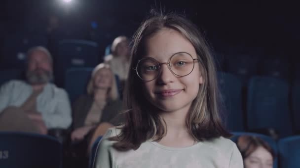 クローズアップポートレートの美しいです白人のPreteen女の子身に着けています眼鏡で映画館に立ってカメラを見て — ストック動画