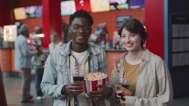身穿休闲装的年轻黑人男子和白人女子的慢幅肖像 在电影院举行约会 手持爆米花 饮料和门票 在镜头前微笑 — 图库视频影像