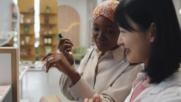 彼女のアジアの友人の新しいスキンケア製品を示す若い黒人女性は 両方の季節の販売中に化粧品スーパーで自己ケアアイテムを表示し テストの前に立っている間 — ストック動画