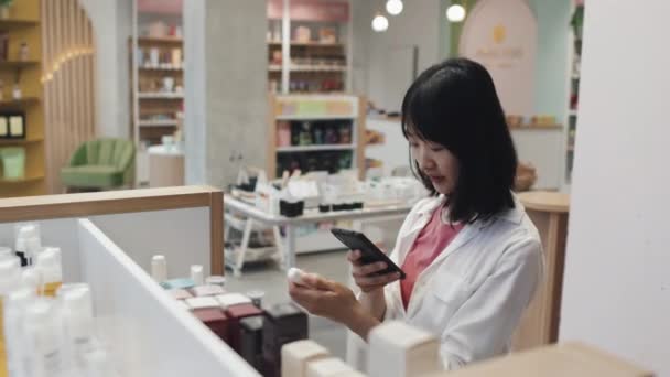 若いアジアの消費者は スキンケア製品を含む小さなボトルを取り 化粧品スーパーでそれらにQrコードをスキャンして 各アイテムについてのオンライン情報を学ぶ — ストック動画