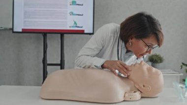 Masada durmuş mankenlerle öğrencilere suni teneffüs yapmayı anlatan olgun bir kadın doktor.