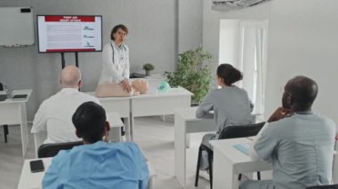 Tıp eğitimindeki öğrencilere kalp masajı yapmayı gösteren beyaz önlüklü olgun bir doktor.