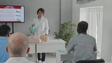 Kalp masajı için torba kapakçığı maskesinin nasıl kullanılacağını gösteren ilk yardım dersi veren bir grup doktor ve hemşireyle çalışan olgun bir sağlık uzmanı.