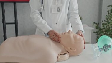 Üzerinde manken olan beyaz önlüklü tanınmayan doktor kalp masajı yöntemleri hakkında konuşuyor.