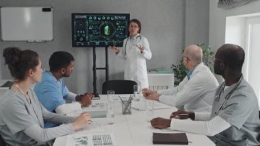 Yeni tedavi yöntemleri hakkında konuşan ve tıp eğitimi sırasında ekranda istatistik gösteren olgun kadın pratisyen.