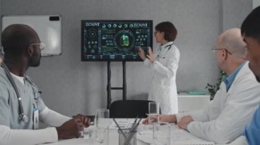 Meslektaşlarının önünde duran olgun kadın doktor tıbbi muayene konuları ve yenilikler hakkında konuşuyor.