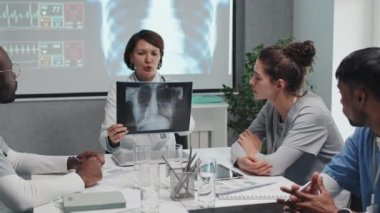 Çok ırklı tıp öğrencileriyle aynı masada oturan olgun kadın doktor onlara röntgen çekimleriyle nasıl çalışacaklarını öğretiyor.