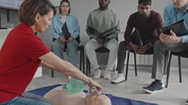 Profesyonel sağlık görevlilerinin yere oturup kalp kapakçığı maskesi ve kalp masajı kullanarak kalp masajı yapmayı öğretmesi.