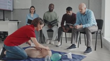 Tıbbi eğitim kursunda suni teneffüs yapmak için yerde oturan olgun bir kadın.
