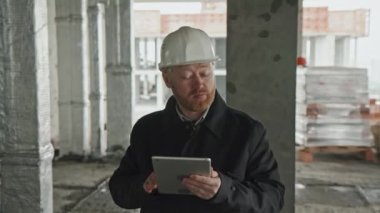 Beyaz ustabaşı siyah ceket giyerken ve inşaat alanında dijital tablet kullanarak yürürken çekilen görüntüler.