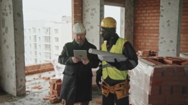 Olgun Kafkasyalı mimar ve Afro-Amerikan inşaat mühendisi dijital tablet ekranı hakkında bilgi okuyor ve çalışma planı hakkında konuşuyor.